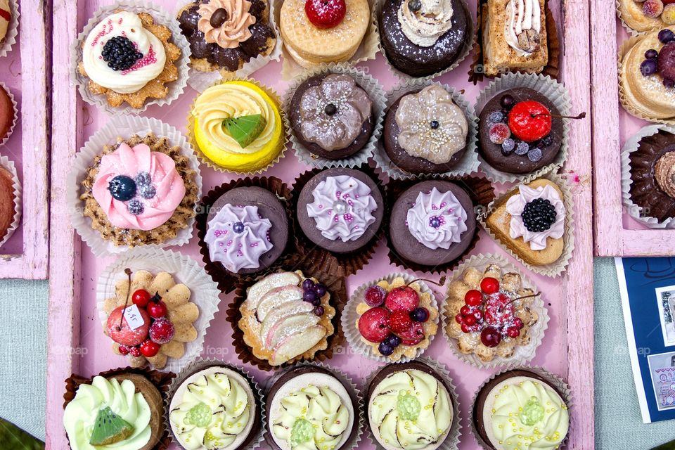 A portrait of a full pink tray of colorful cupcakes. the pastries really look delicious.