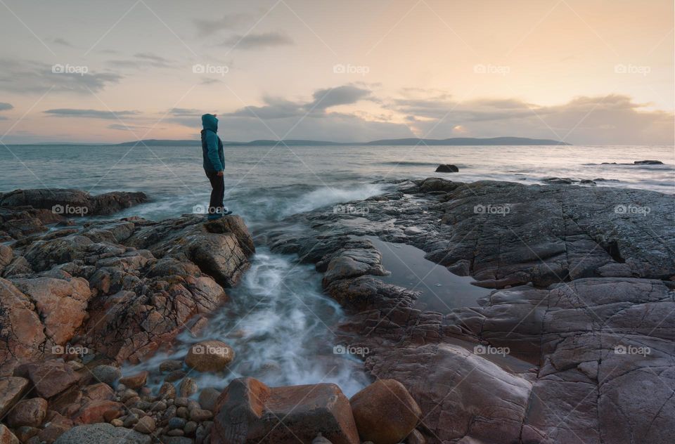 Sunset with man standing on the rocky coast of Wild atlantic way in Galway, Ireland