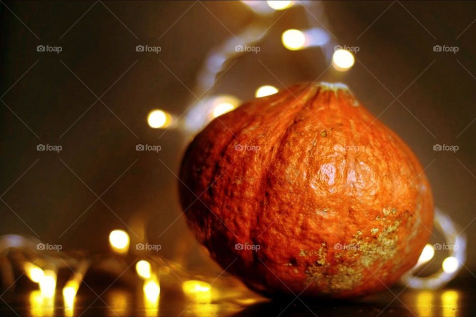 An orange Hokkaido pumpkin on black table surrounded and illuminated by a string of lights