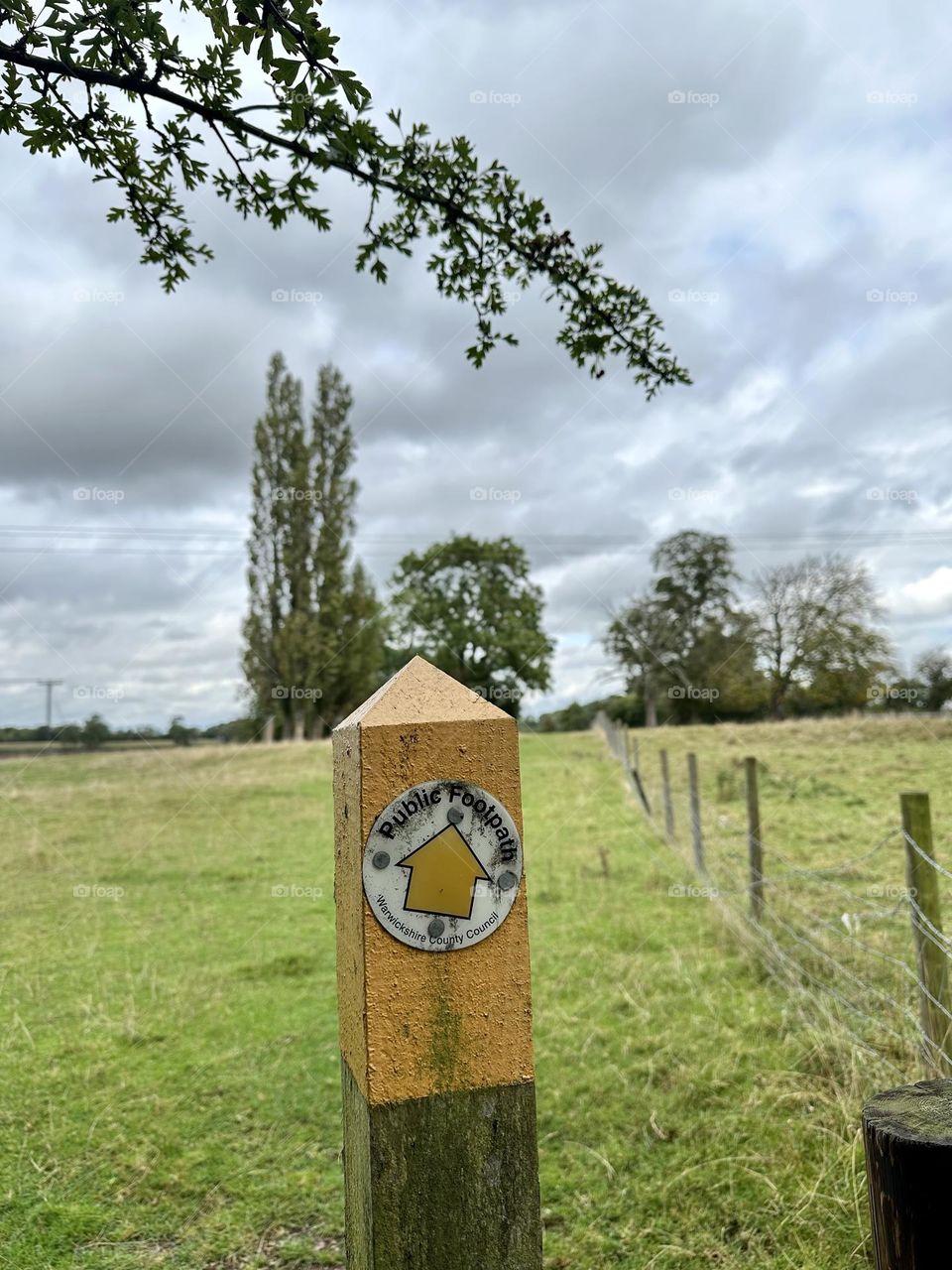 Public footpath walkway marker by church of St. James in Ansty near Coventry England along oxford canal tree line fence field cool sky clouds just before rain weather