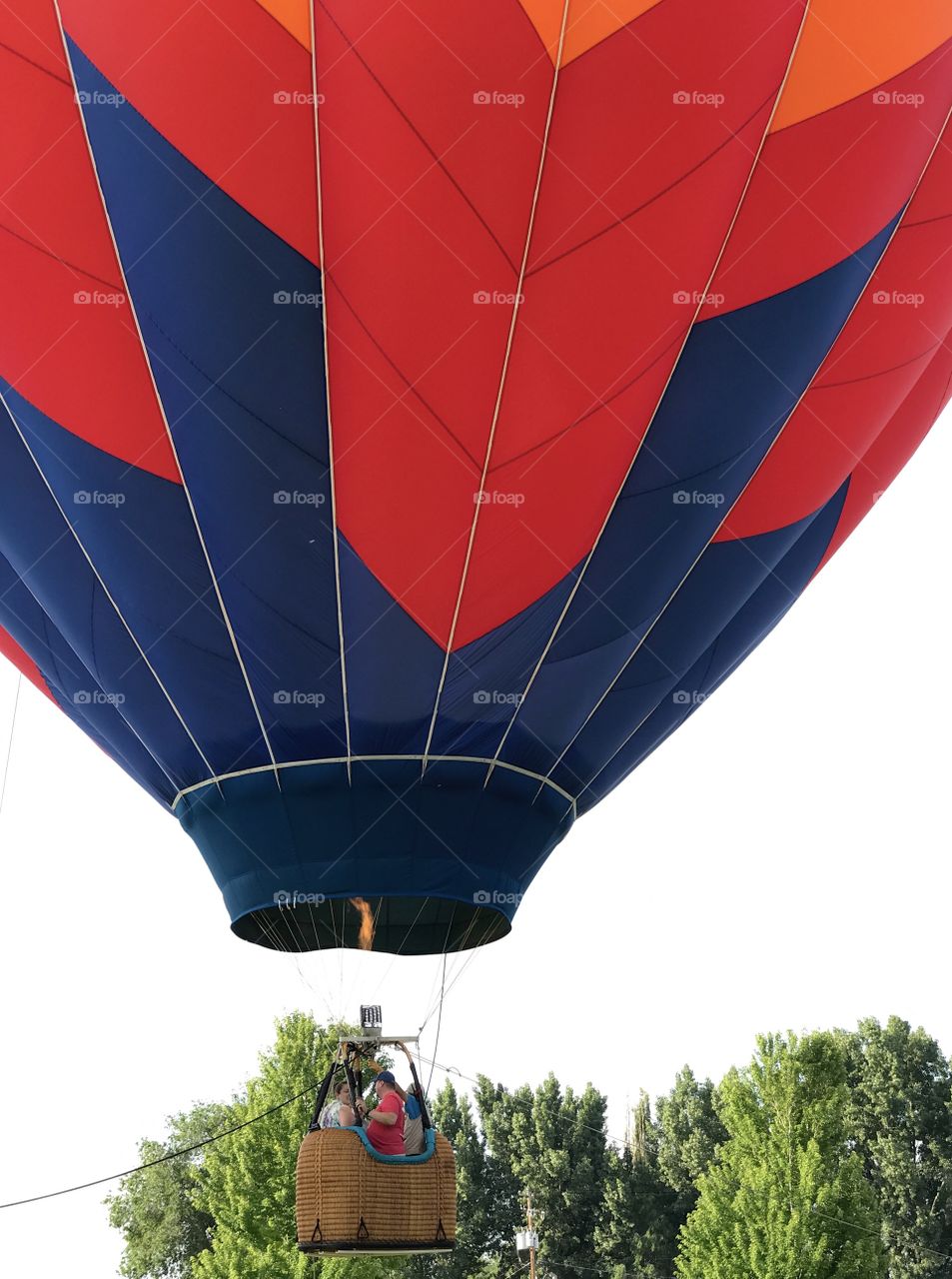 A hot air balloon with brilliant colors ascends on its morning flight with a nice flame and a happy family taking a ride in Ochoco Park in Prineville in Central Oregon on a summer morning in July. 