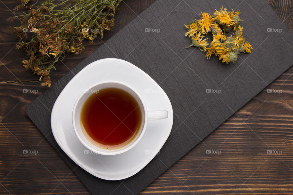 cup of herbal tea on slate board on a wood table. calendula and St. John's wort grass
