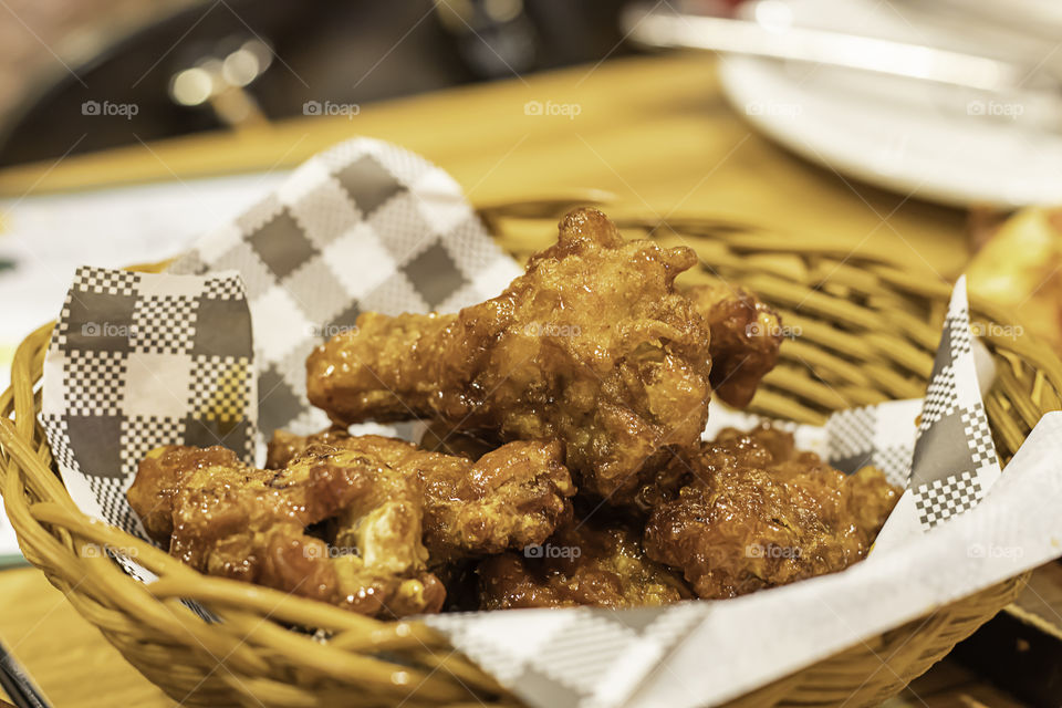 Fried chicken, sweet and sour sauce in a wicker basket on a wooden table.