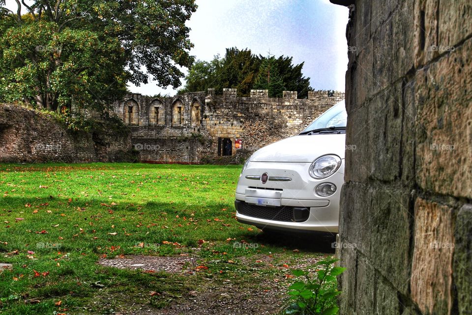 Fiat 500 Peekaboo. A white Fiat 500 peeks out from the side of a wall with historic buildings in the background.