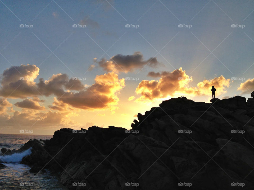 Figure silhouetted on the rocks at sunset