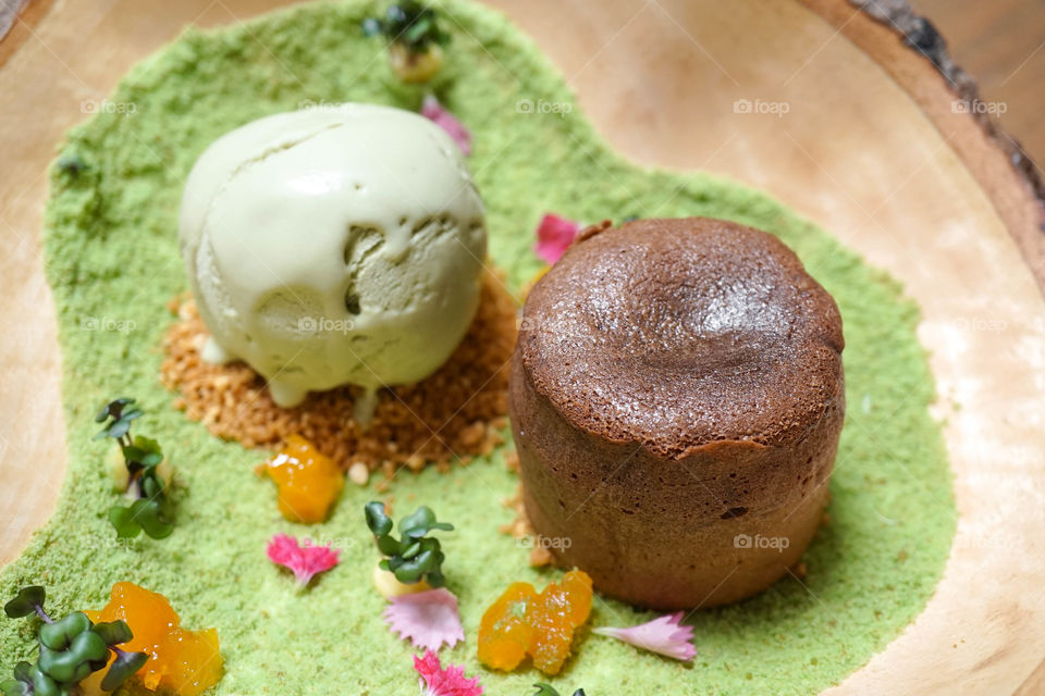 chocolate lava cake with matcha green tea ice cream on wooden plate decorated in เa secret garden concept, creative idea. Selective focus on top of chocolate cake.