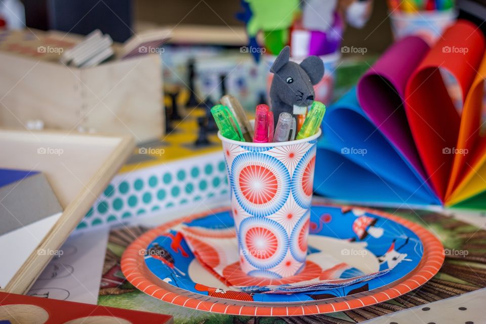 Pens and a finger puppet in a cup on a plate