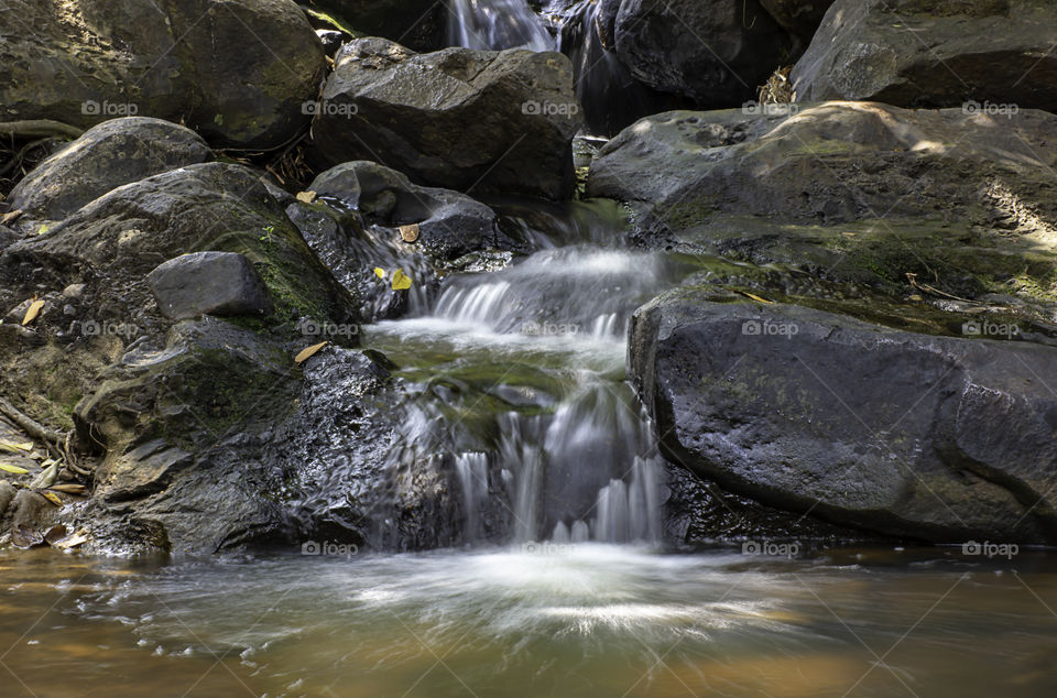 The water flowing over rocks and trees down a waterfall at Khao Ito waterfall , Prachin Buri in Thailand.