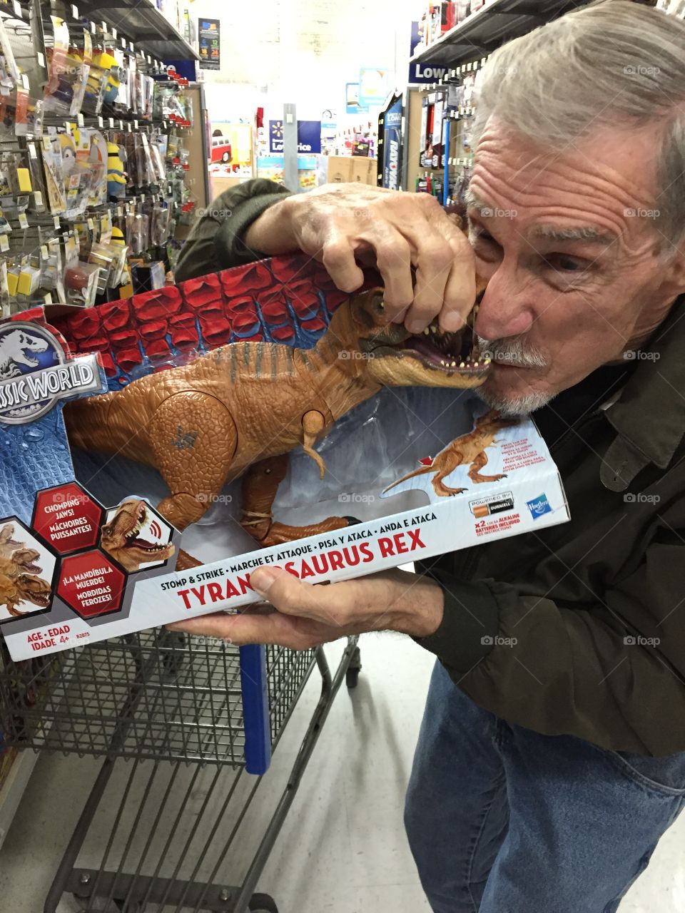 Man in a store toy aisle and pretending to bite a T. rex dinasour. And having fun.