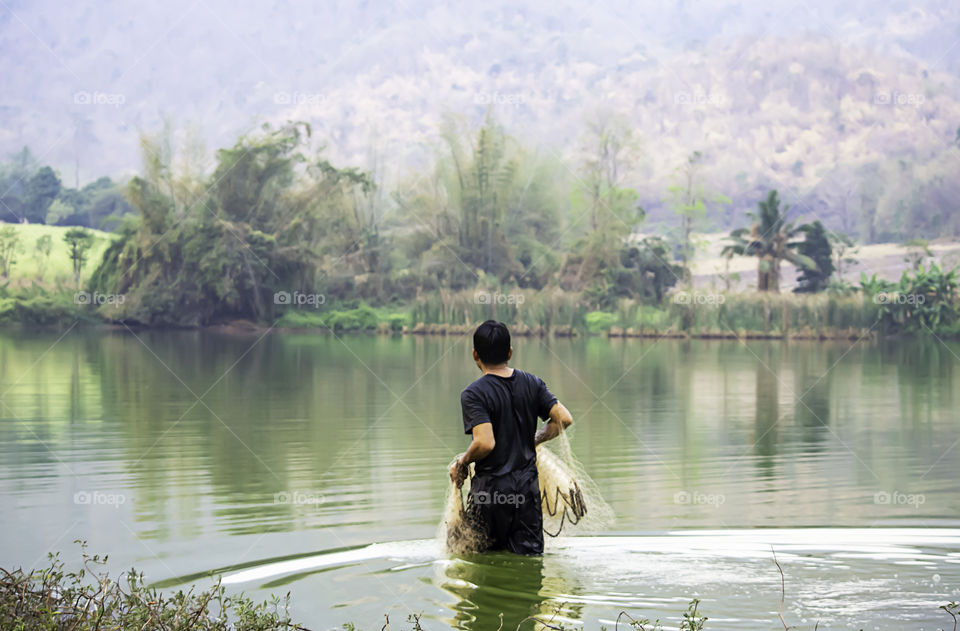 Man holding fishing nets walking in water Background blurred mountains and trees