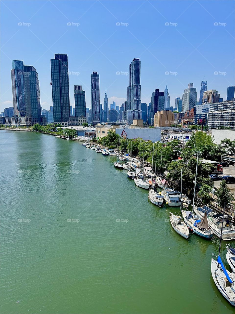 This lovely harbor motif unfolds overlooking “Newtown Creek” with its many boats from the “Pulaski Bridge” that connects “Greenpoint”, Bklyn to LIC. “Manhattan” including the “Empire State Bldg” is visible in the distance. 2024. Hypnotic Productions