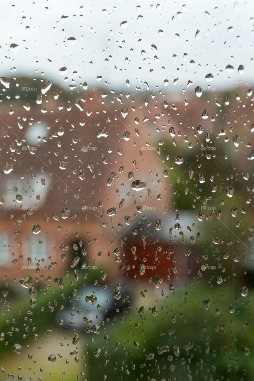 Photo of a red brick house and a car taken through a wet window. Focus on rain drops. Green plants next to the house