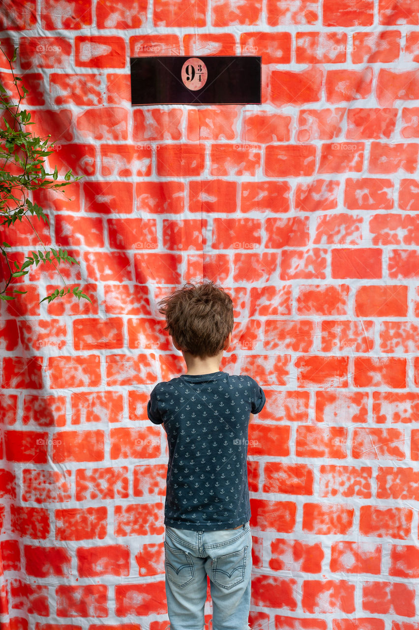 Little boy standing in front of brick wall.