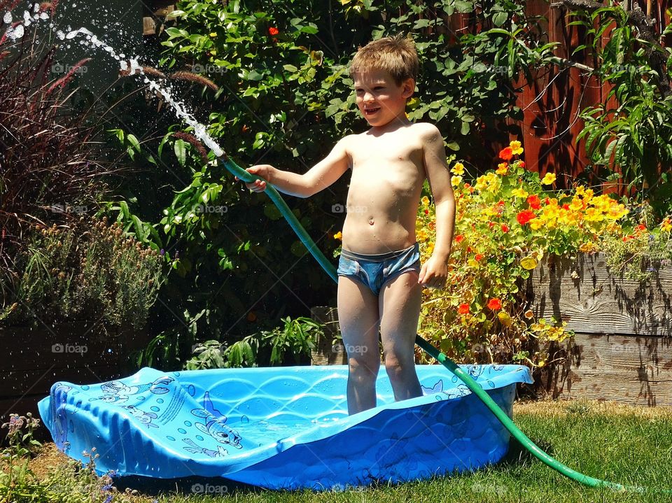 Boy Spraying Water. Young Boy Spraying A Hose In The Pool On A Hot Summer Day
