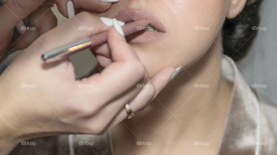 Makeup artist makes makeup to the bride. Beautiful, healthy skin. The lips are painted with natural lipstick. In the hands of a makeup artist, a lip pencil.