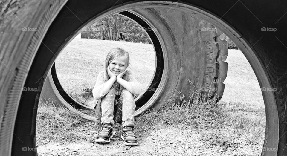 black and white photo of a child sitting near a tire.