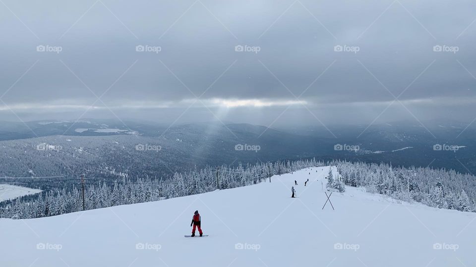 The outgoing ray of the sun shines through the clouds on the ski slope