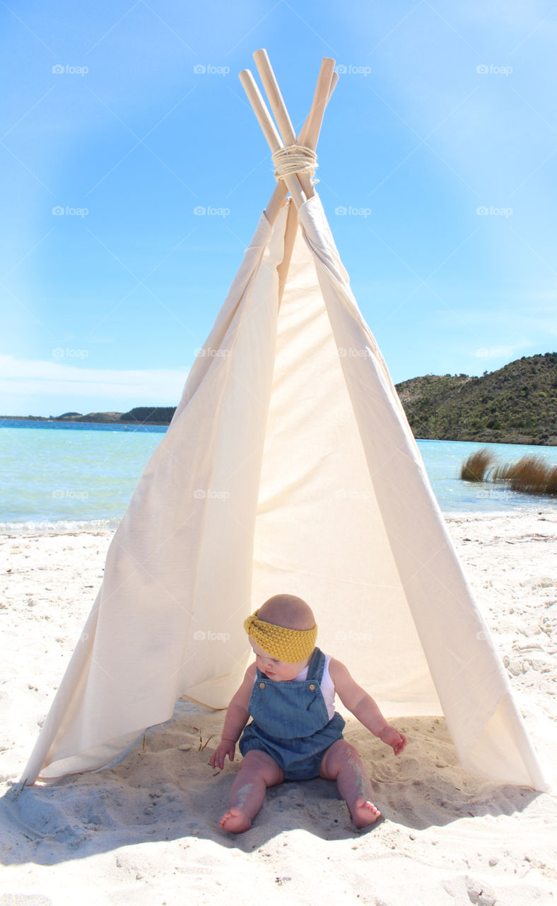 little girl playing in the sand under a tepee
