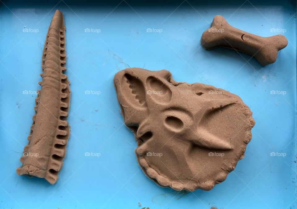 Top view of a child’s triceratops dinosaur sand sculpture on a blue background. 