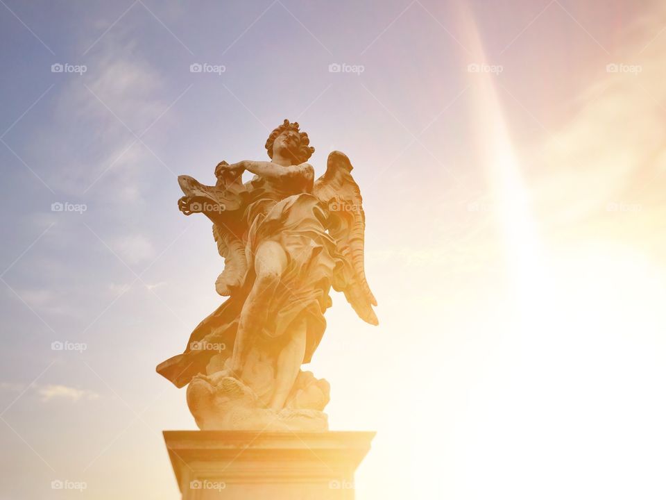 marble statue of an angel with the sun in backlight at sunset