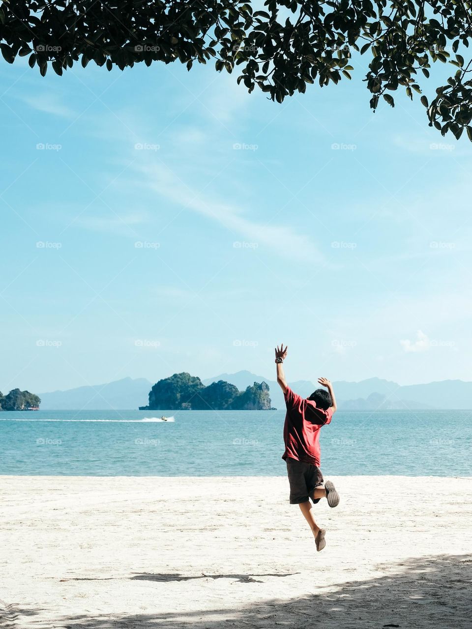 A young boy jumping with joy in the sunshine on the beach of Langkawi Tanjung Rhu, Malaysia