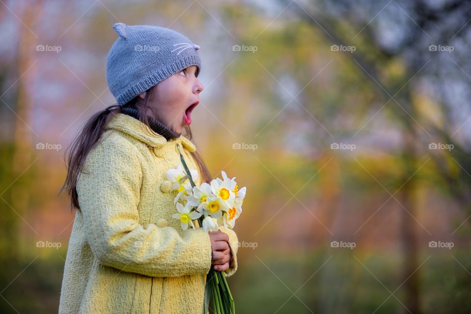 Little girl with narcissus bouquet in spring park.