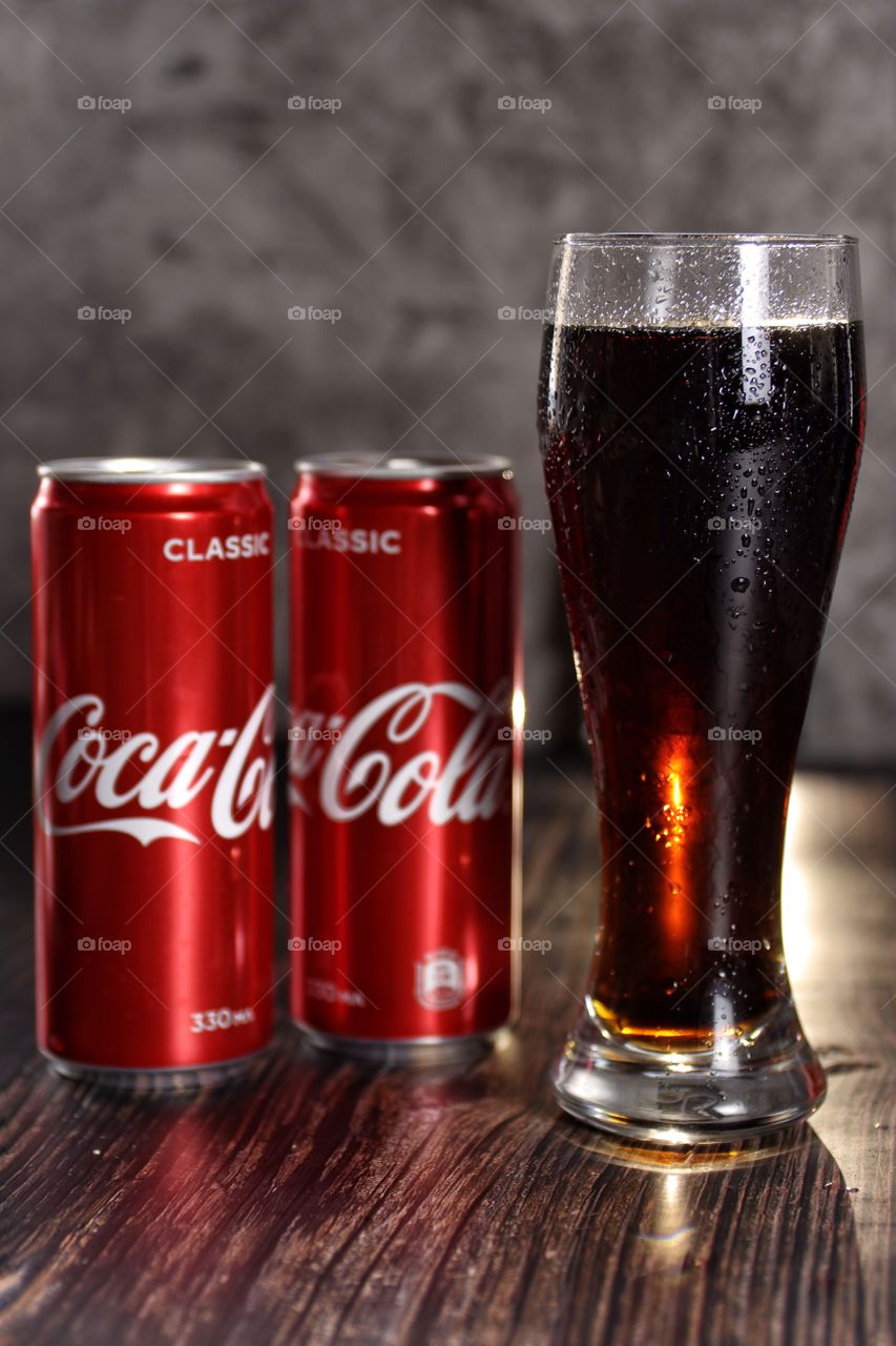 a glass of Coca-Cola and two metal cans