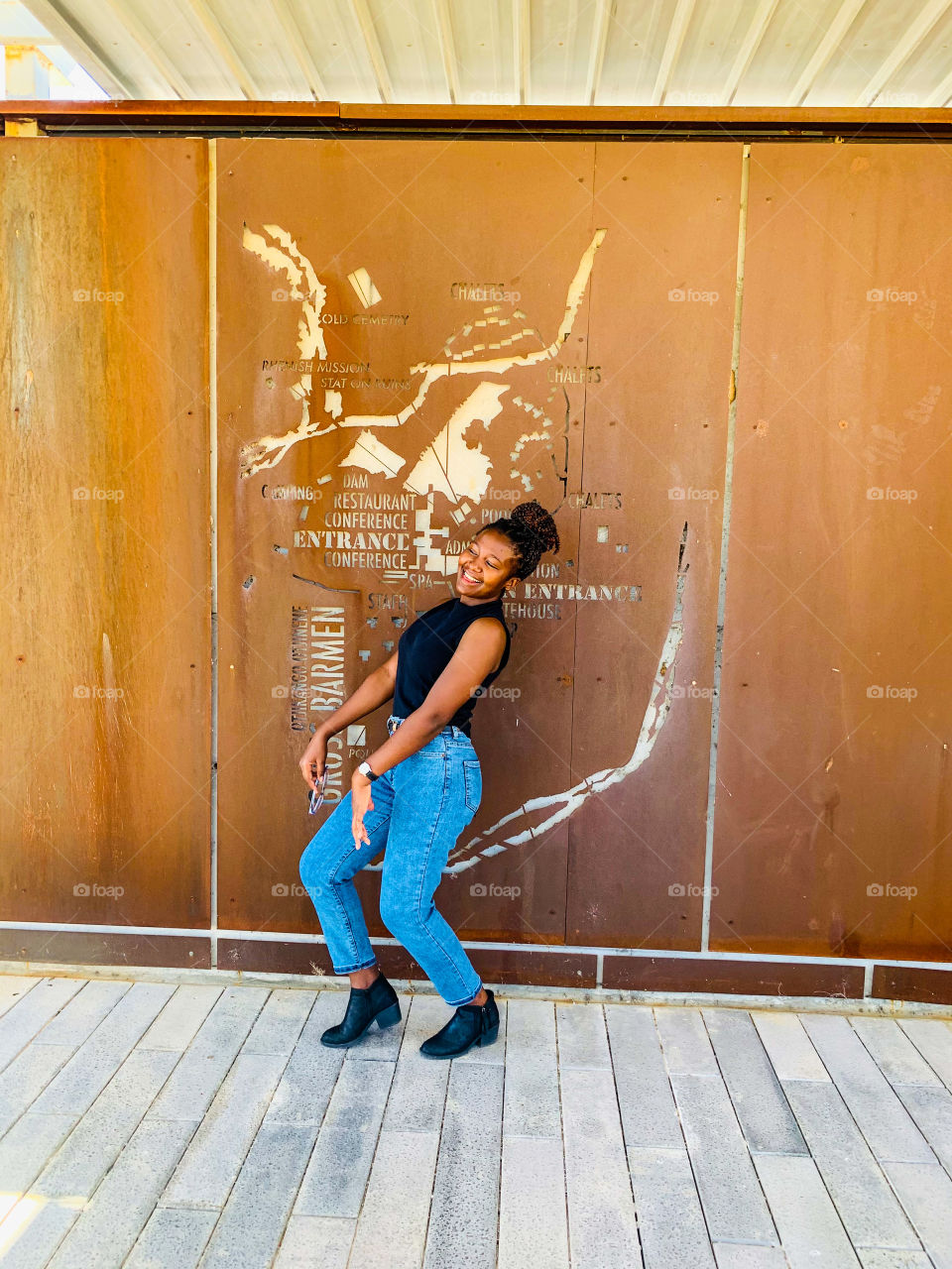 A young black lady laughing and dancing in joy at a brown metal wall map.