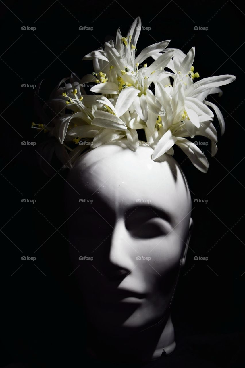 white ceramic mannequin head with faux flowers on top low key photography black background