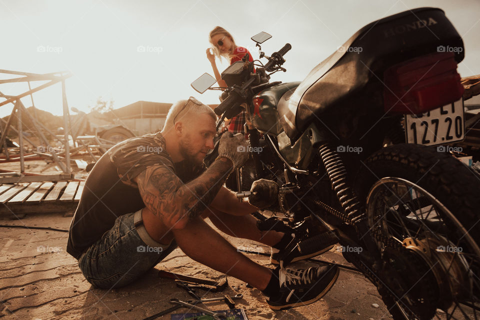 guy and girl repair a motorcycle at sunset