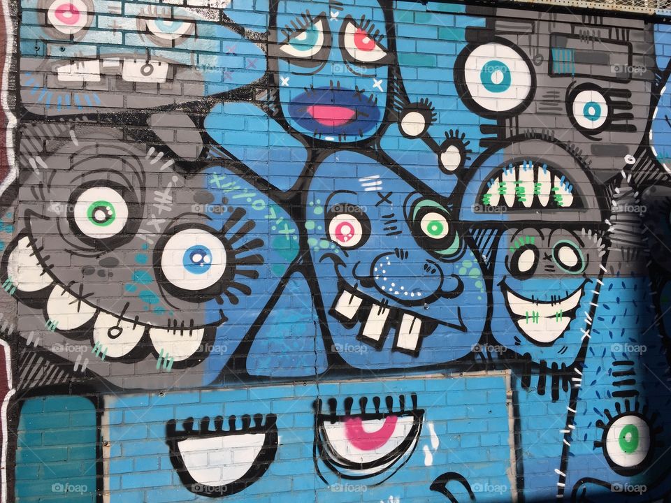 Blue and grey spray paint pigment figured into unique individual emojis . Artistic techniques are visible. Painted on a Brooklyn building .