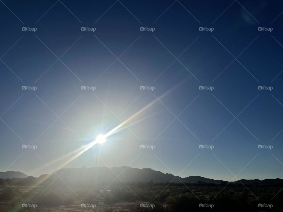 A clear sky with the sun shining and mountains. 