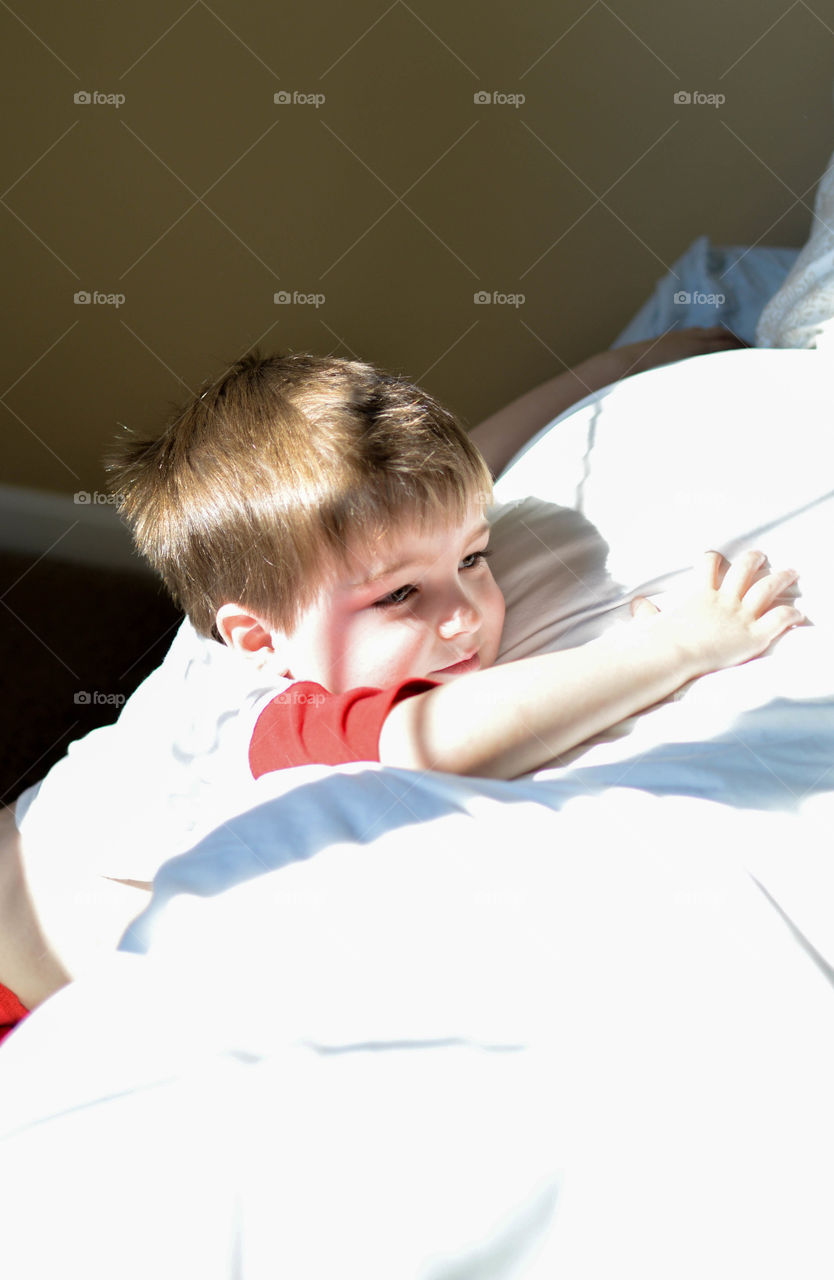 Young toddler boy resting on a cushion indoors with shadow lines running across him from natural light coming in through a window