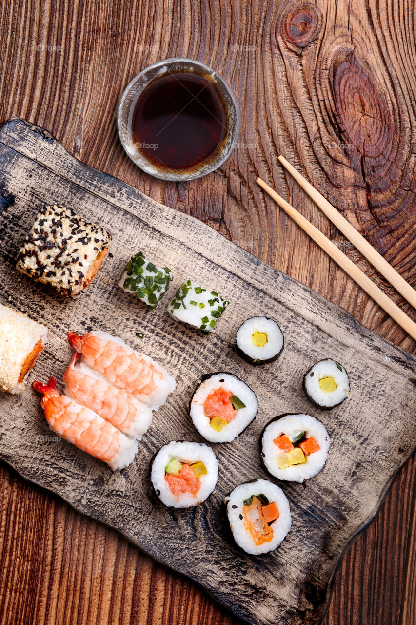 Sushi set on pottery plate with chopsticks and soy sauce in bowl on old wooden table from above