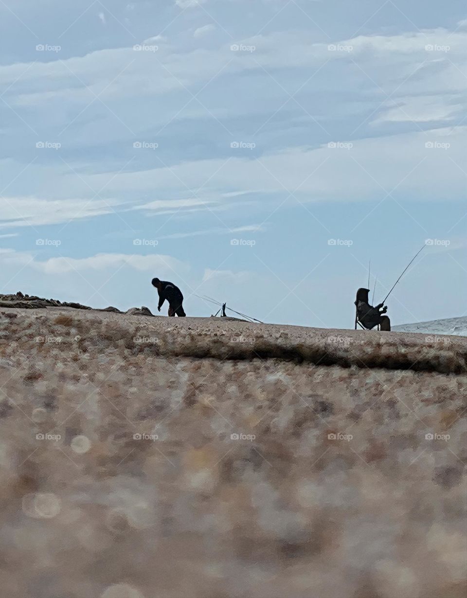 Fishermen at the Atlantic Ocean beach seashore relaxing and fishing on a little sand hill by the salty water.