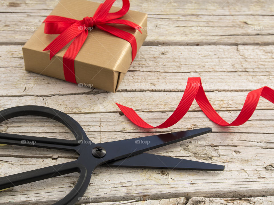 Gold present with red ribbon and black scissor on vintage wooden table 