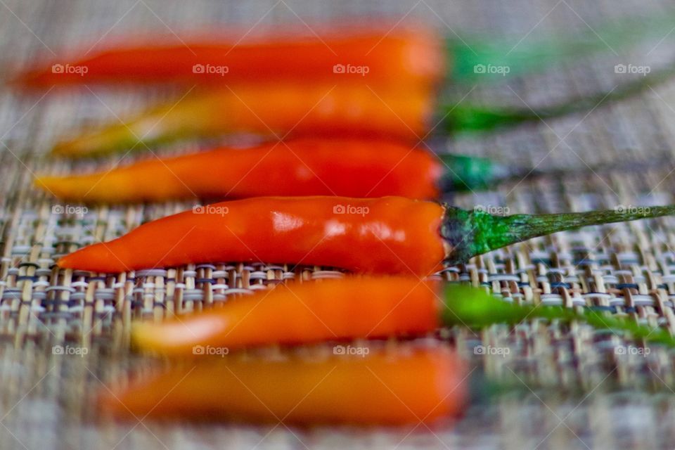 Angled closeup view of Thai Bird’s Eye / Thai Bird Chili peppers arranged by size on a woven neutral background