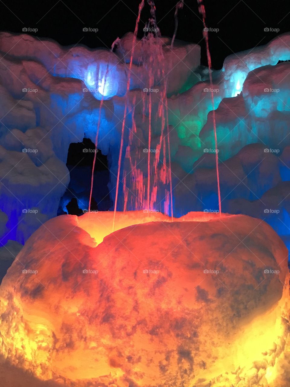 Ice Castle with beautiful fountain and colorful lights in the ice. It has hues of green, blue, and red. It is in Lincoln, New Hampshire.
