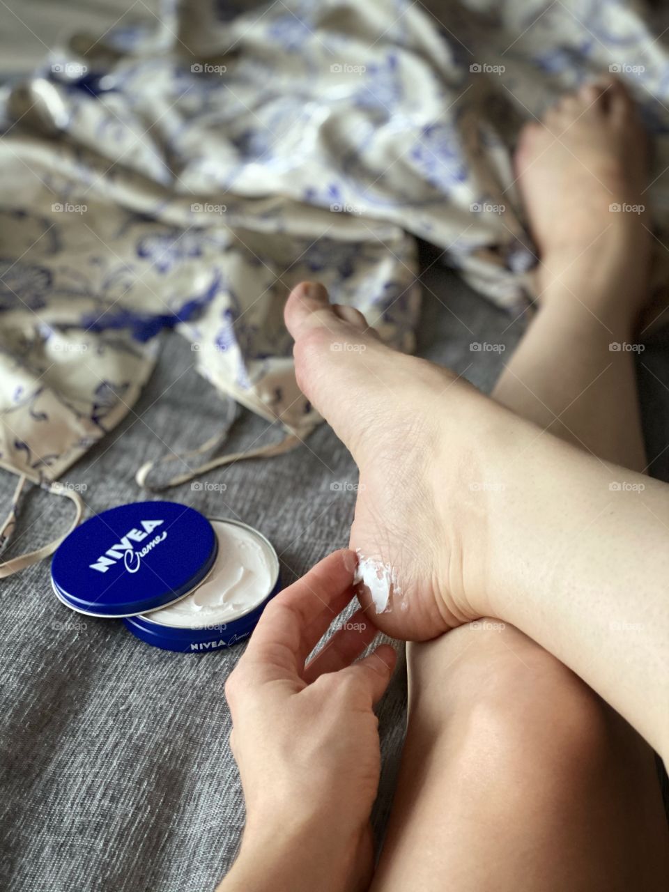 using Nivea cream to soften the skin of the heels.  Image of body parts of hands and feet in daylight on chemise background
