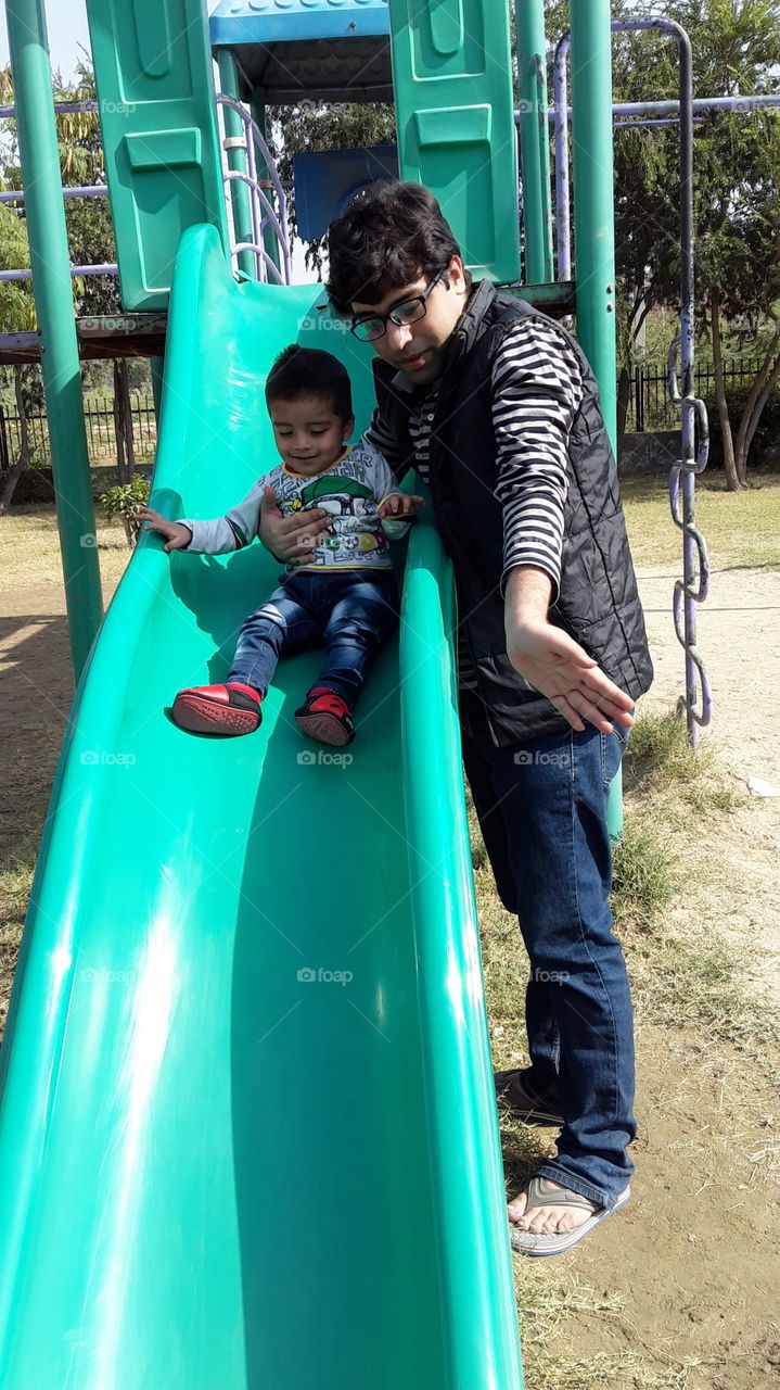 Cute boy enjoying the sliding swing in the park with his uncle