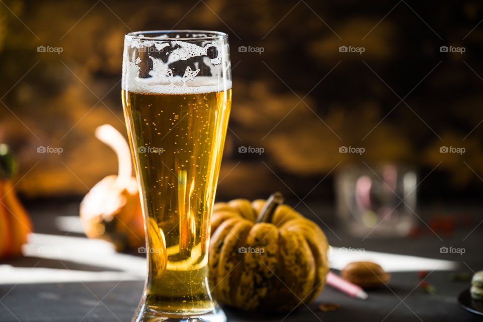 golden beer in a glass on rustic, black table next to autumn decorations