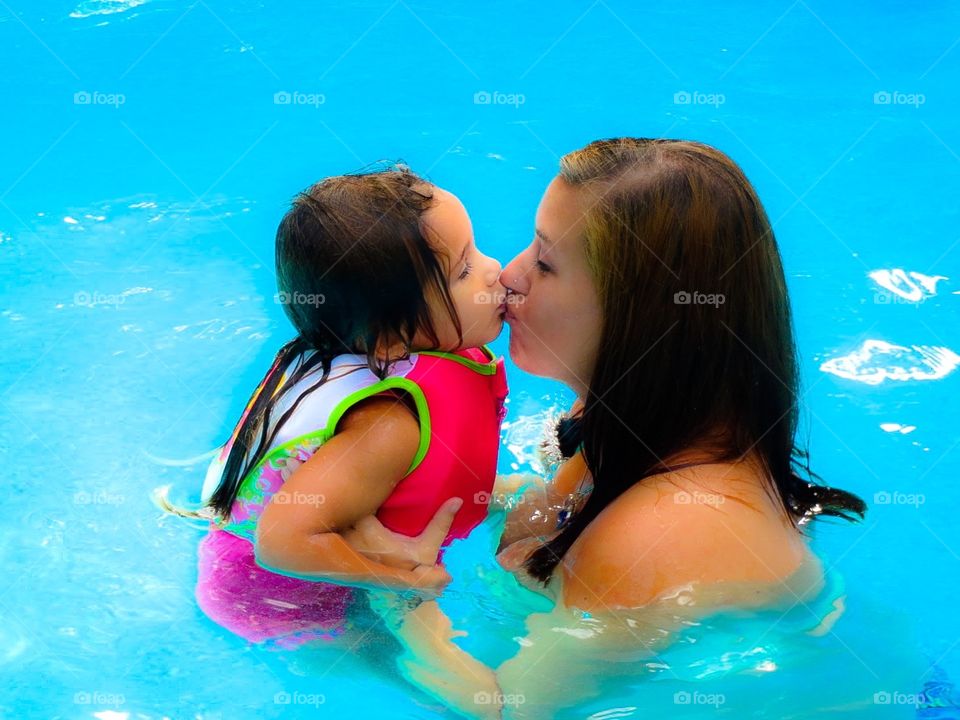 Wet Kisses. mother and adorable daughter giving sweet kisses at play in the pool on a hot summer day