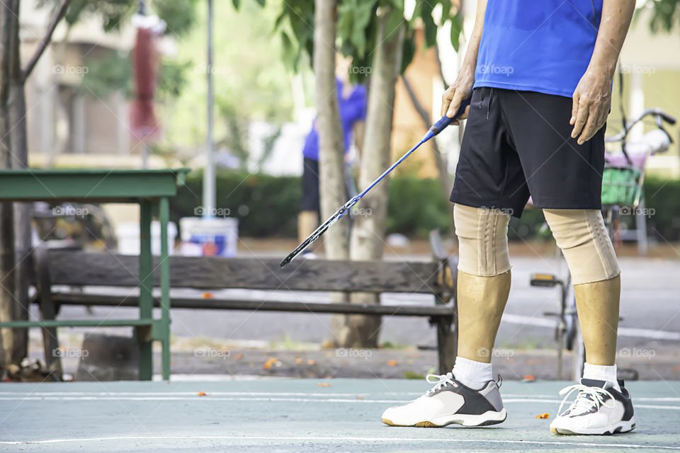 Elderly man Hand holding a badminton racket Background blur tree in park.