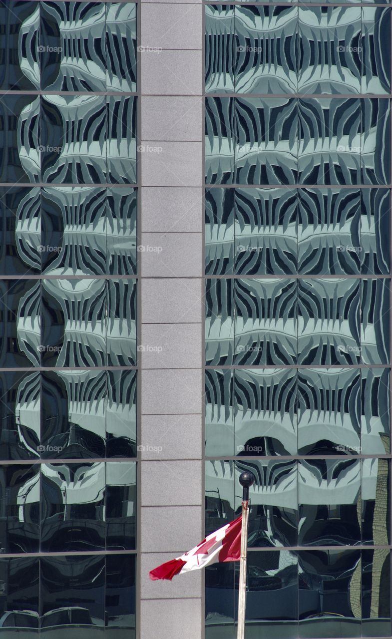 The side of an office building in Regina, SK, CA.  The glass is imbued with patterns.  A limp Canadian flag hags in the foreground.