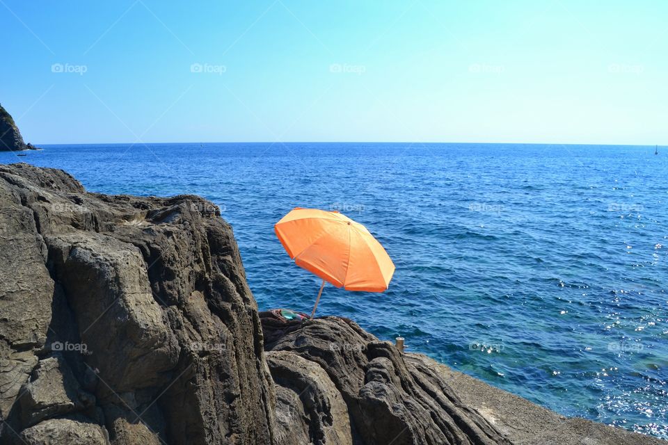 Orange umbrella on rocks at sea