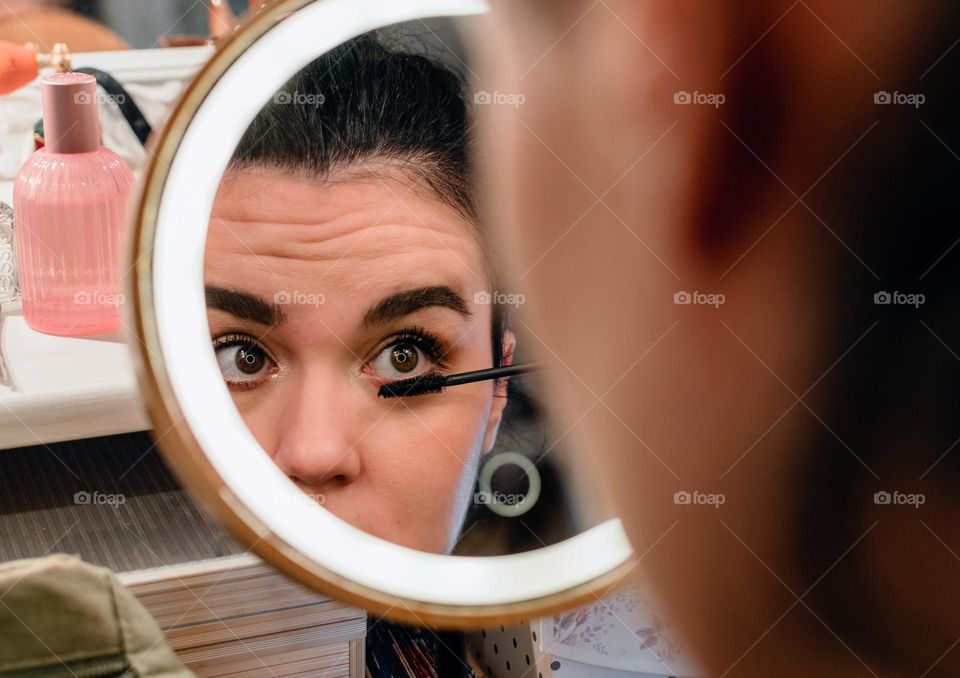 Portrait of young woman doing her make-up in front of circular led illuminated mirror