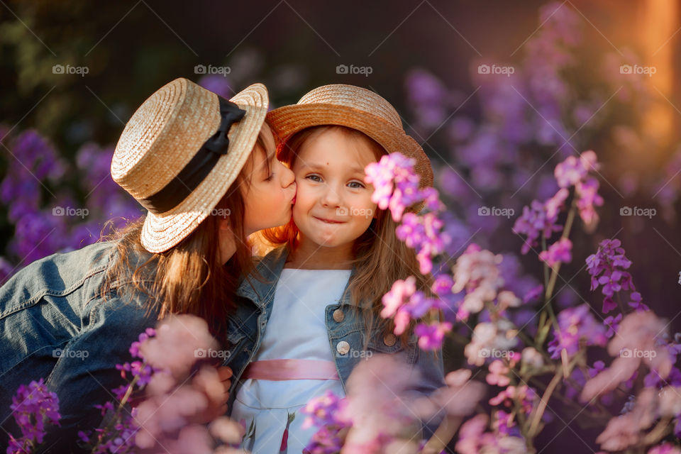 Little sisters in a blossom meadow at sunset 