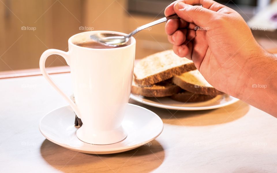 Person holding spoon with tea cup