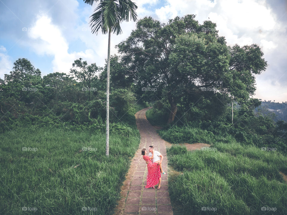 The couple is enjoying a Bali vacation and walking along the path in a beautiful park.