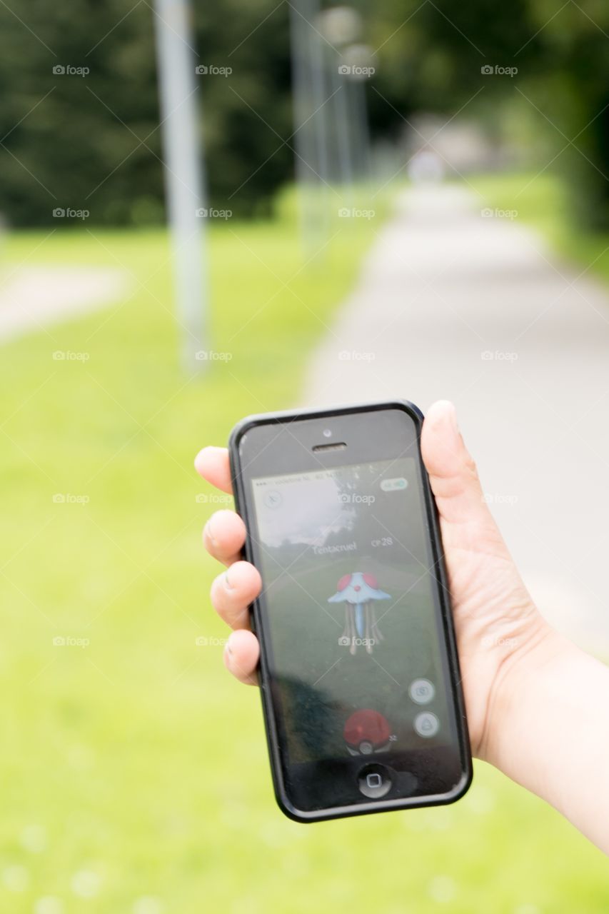 A hand holding an iPhone while playing Pokémon-go